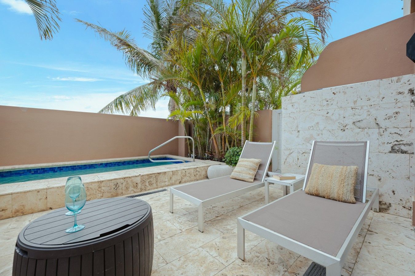 A rooftop pool area with lounge chairs, a small table with a glass, and a clear view of the sky.