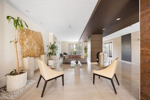 A spacious living area with a sofa set, two armchairs, and a coffee table. There are potted plants and a large abstract wall art piece. - Luxe Beach Condo Le Vent Townhouse 17 by Bocobay (Noord)
