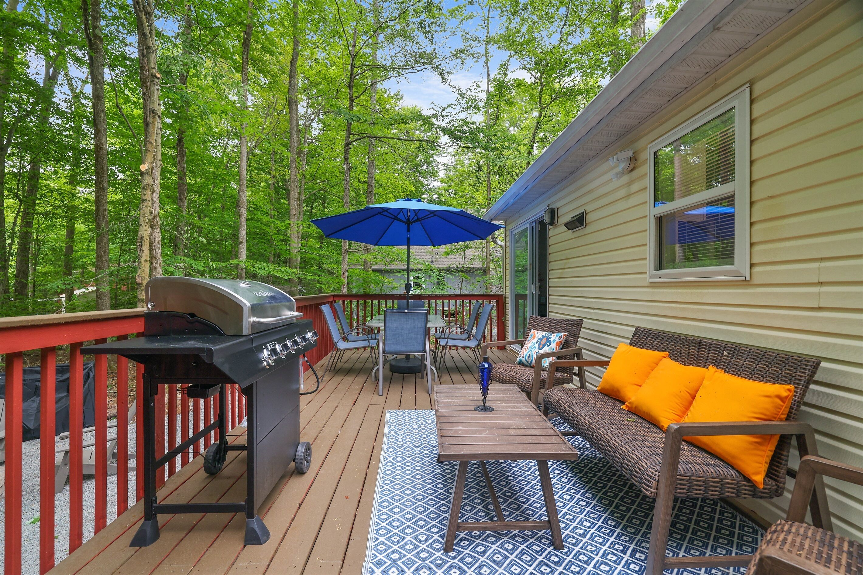 A deck with a grill, outdoor furniture, and a blue umbrella.