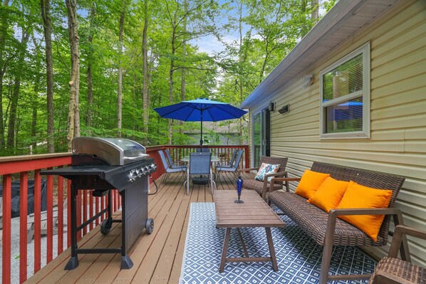 A deck with a grill, outdoor furniture, and a blue umbrella.