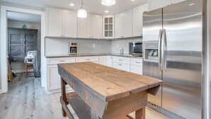 A modern kitchen with white cabinetry, a stainless steel refrigerator, and a wooden island table. - Steps to Beach: Cape Cod Family Retreat w/ Patio (Bourne)