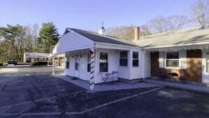 A small, single-story building with a gabled roof, a porch with blue chairs, and a small table. - The Cutler 1-bedroom · Near Mystic, Casinos + USCGA (Groton)