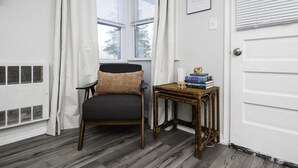 A room with a chair, a small table with books, and a window with white curtains. - The Cutler 1-bedroom · Near Mystic, Casinos + USCGA (Groton)