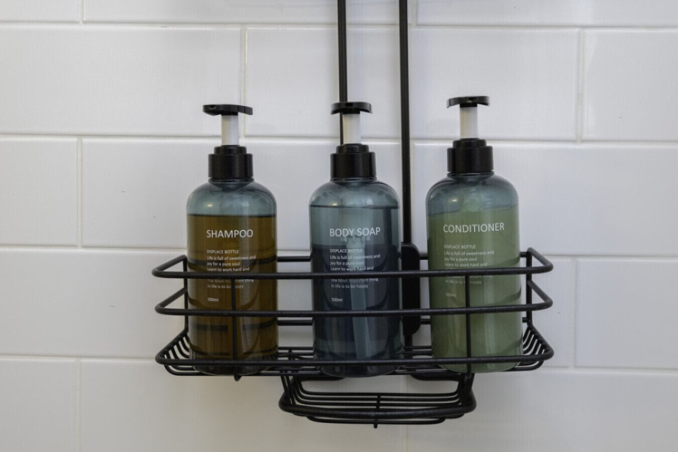 En hylder i badeværelset med tre flasker shampoo, kropssæbe og balsam.