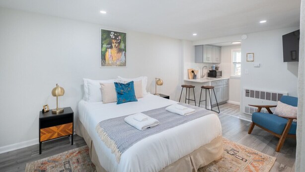 Une chambre moderne avec un grand lit, un petit bureau et, au fond, un coin cuisine.