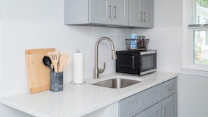Une cuisine moderne avec des meubles gris, un évier en acier inoxydable, un micro-ondes noir et une planche à découper en bois avec des ustensiles.