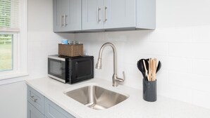 A kitchen with light blue cabinets, a stainless steel sink, a microwave, and a basket on the counter. - The Rossie Studio · Near Mystic, Casinos + USCGA (Groton)