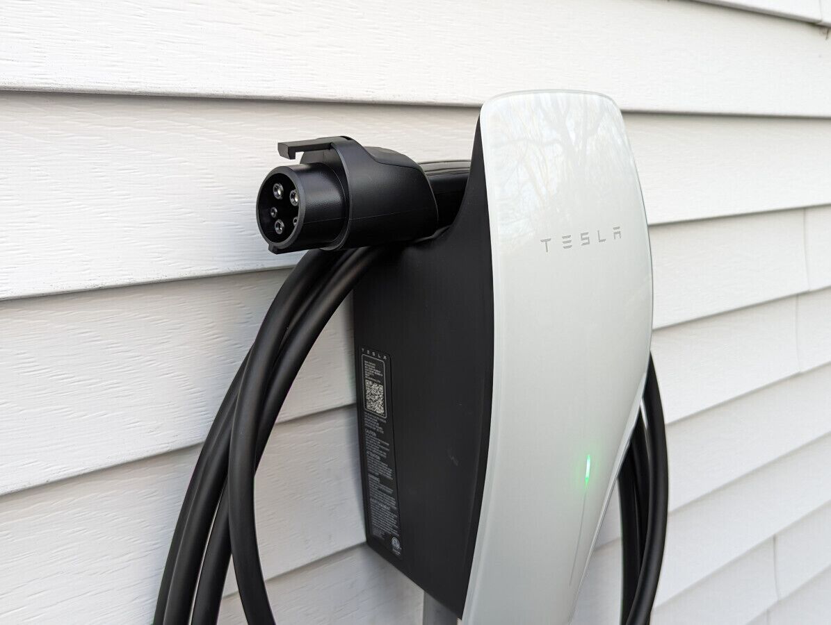 Een Tesla laadstation bevestigd aan een witte buitenmuur.