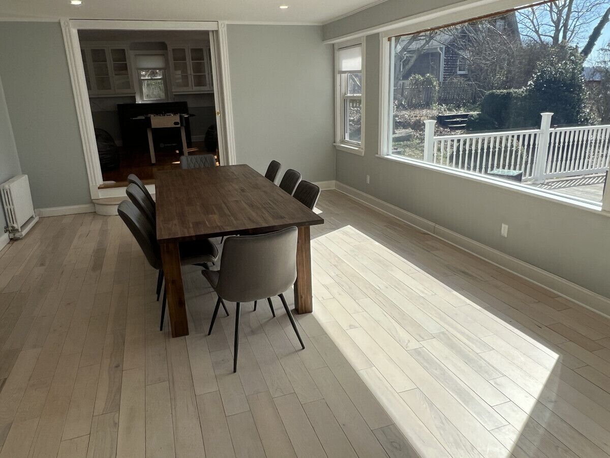 A spacious dining area with a wooden table and chairs, large windows, and a view of the backyard.