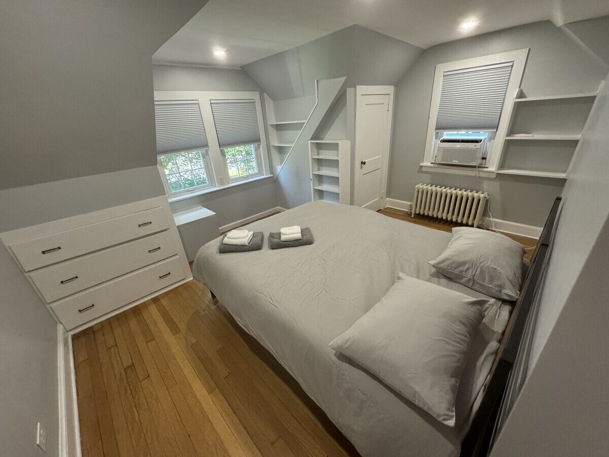 A bedroom with a bed, a dresser, a radiator, and a window with blinds.