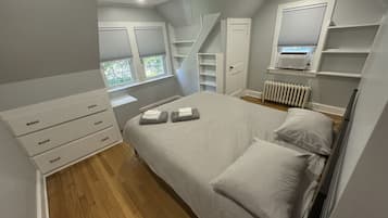 A bedroom with a bed, a dresser, a radiator, and a window with blinds.