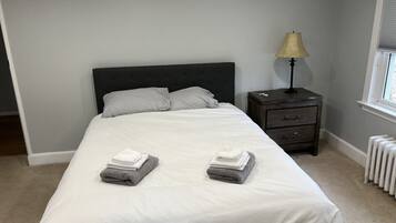 Ein ordentlich bezogenes Bett mit zwei gefalteten Handtüchern, ein Nachttisch mit einer Lampe und eine Heizung.