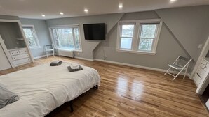 Een slaapkamer met een groot bed, houten vloeren, een aan de muur bevestigde televisie en een raam met uitzicht op bomen.