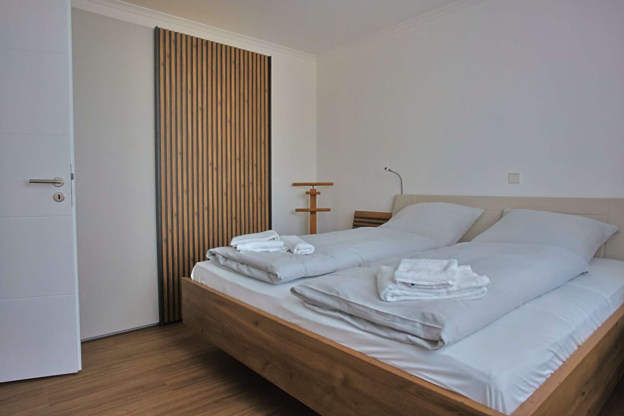 Un dormitorio con cama de madera, ropa de cama blanca, un armario de madera y una puerta con mirilla.