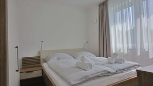 A modern hotel room with a wooden bed frame, white bedding, and a view of the outdoors through sheer curtains. - Villa Baltic Star Ferienwohnung 10 (Börgerende-Rethwisch)
