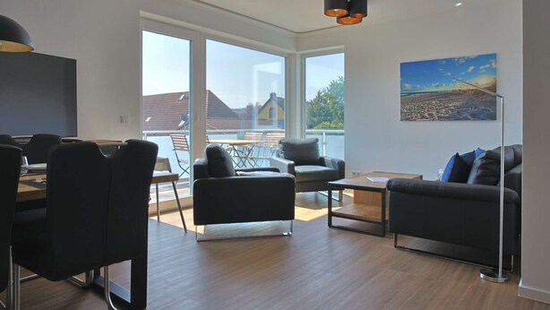 A modern living room with a large window, a dining area, and a sofa. - Villa Baltic Star Ferienwohnung 10 (Börgerende-Rethwisch)