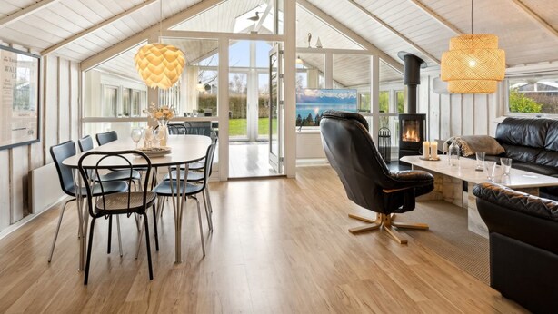 A spacious room with a high ceiling, a dining area with a table and chairs, a black leather sofa, a fireplace, and large windows offering a view of the outdoors. - "Chrisse" - 250m from the sea by Interhome (Otterup)