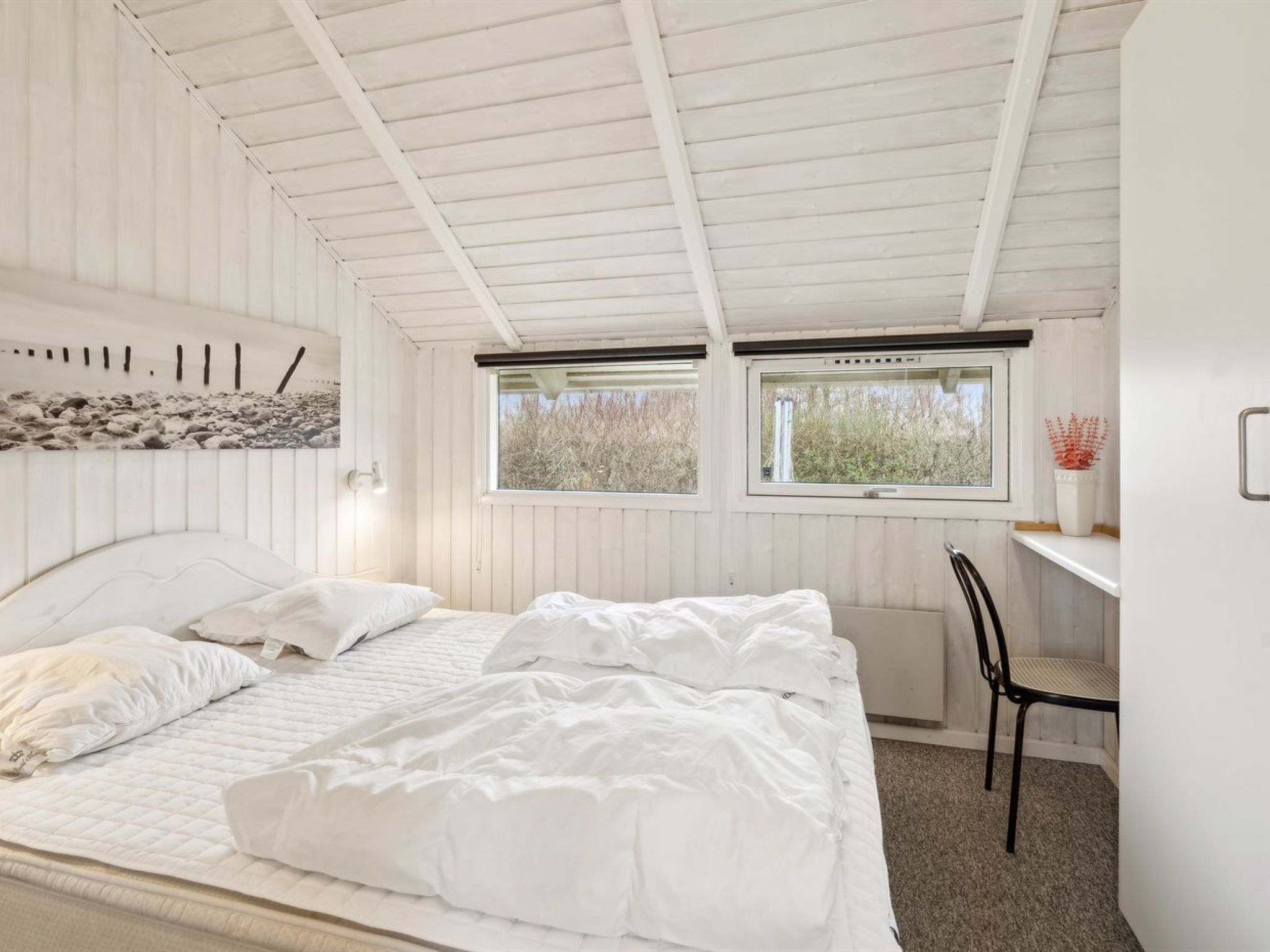 A bedroom with a bed, two windows, a desk, and a chair.