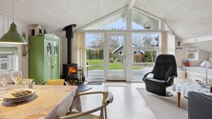 A cozy attic room with a wood-burning stove, a dining table with chairs, a black leather chair, and a view of the backyard. - "Hereth" - 100m from the sea by Interhome (Otterup)
