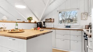 Een moderne keuken met witte kasten, een houten aanrecht en een groot eiland. Er staat een koffiezetapparaat, een spoelbak en diverse keukenbenodigdheden op het aanrecht.