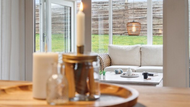 Een moderne woonkamer met een groot raam, een witte bank, een bijzettafeltje en een kaars op een dienblad.