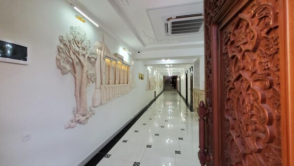 A hallway with a polished floor, wall-mounted light fixtures, and a decorative wooden door.