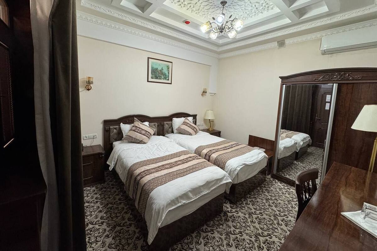 Una habitación de hotel con dos camas, un escritorio de madera, un espejo y una alfombra estampada.