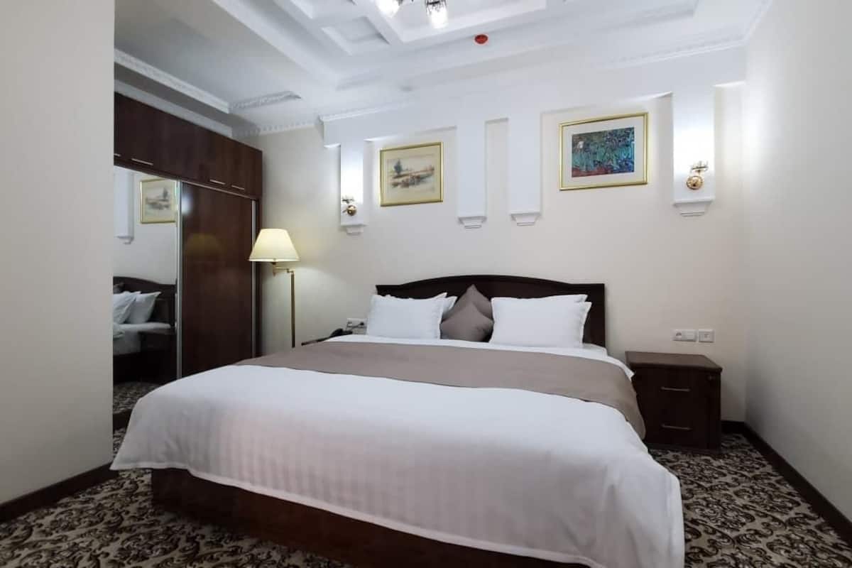 Una habitación de hotel con una cama grande, un armario, una mesita de noche y una lámpara.