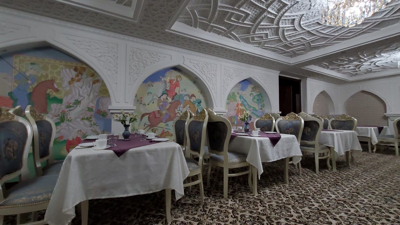 A dining area with ornate ceiling and wall murals, white tablecloths, and classic chairs.