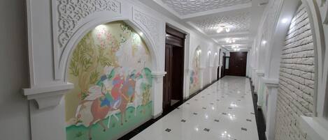 A hallway with ornate white walls, a tiled floor, and a mural of colorful horses.