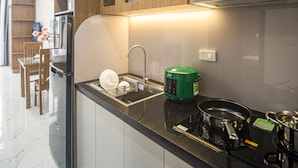A modern kitchen with wooden cabinets, a black countertop, and a built-in stove. - Confetti Apartment (Hanoi)