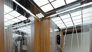 A modern elevator with a checkered floor pattern, metal railings, and a glass ceiling. - Confetti Apartment (Hanoi)