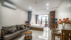 A modern hotel room with a sofa, a small round table, a bed, a dining table with chairs, and a balcony with a railing. - Confetti Apartment (Hanoi)