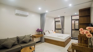 A modern hotel room with a bed, a sofa, a small table, and a wooden cabinet. - Confetti Apartment (Hanoi)