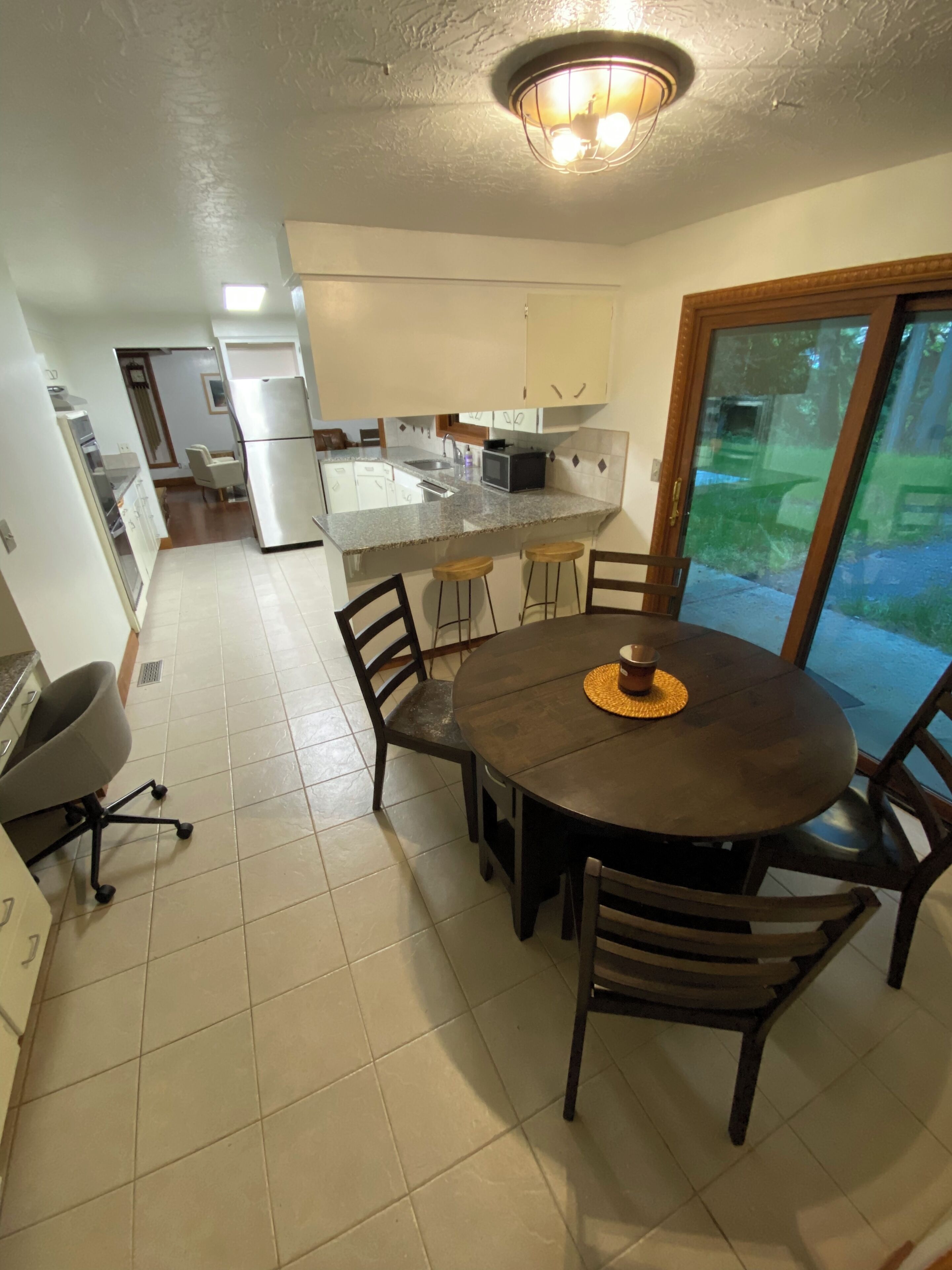 Une cuisine moderne dotée d’un îlot central, d’un coin repas avec une table ronde et des chaises, et d’une porte-fenêtre coulissante donnant sur un jardin.