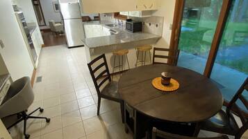Une cuisine moderne dotée d’un îlot central, d’un coin repas avec une table ronde et des chaises, et d’une porte-fenêtre coulissante donnant sur un jardin.