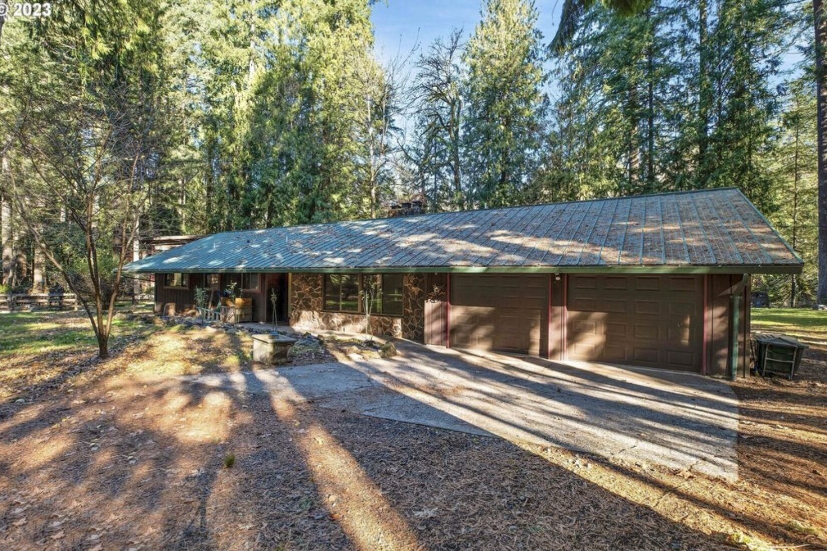 Une maison à deux étages avec un garage, entourée d’arbres et bordée d’une allée en gravier.
