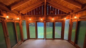 Een kamer met een hoge plafond en houten balken, grote ramen met groen gekleurd glas en een betonnen vloer.