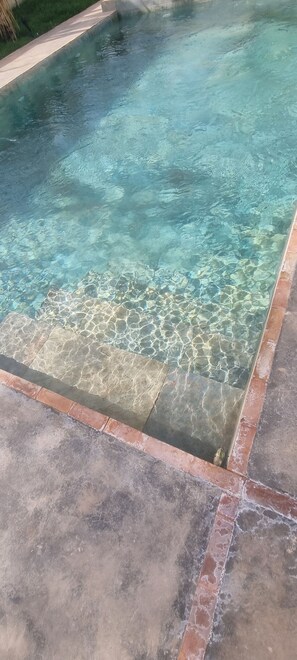 Une piscine aux eaux cristallines, bordée de carreaux et dotée d’une terrasse en béton.