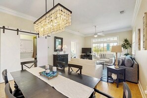 Un coin repas avec une table en bois foncé, un lustre et une vue sur un salon comprenant un canapé et un téléviseur.