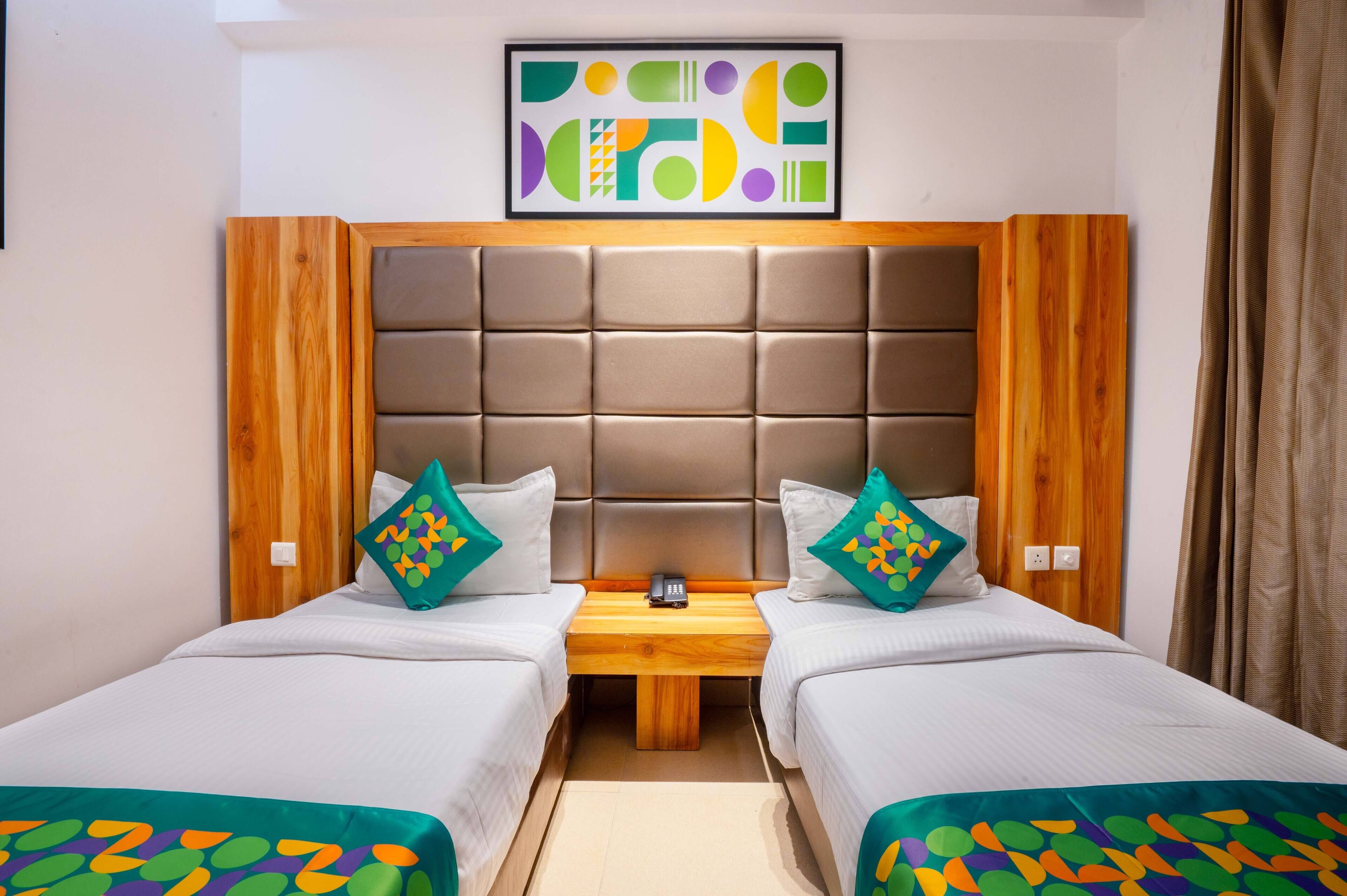 A hotel room with two beds, a wooden headboard, a small wooden table with a phone, and a colorful abstract painting above the beds.