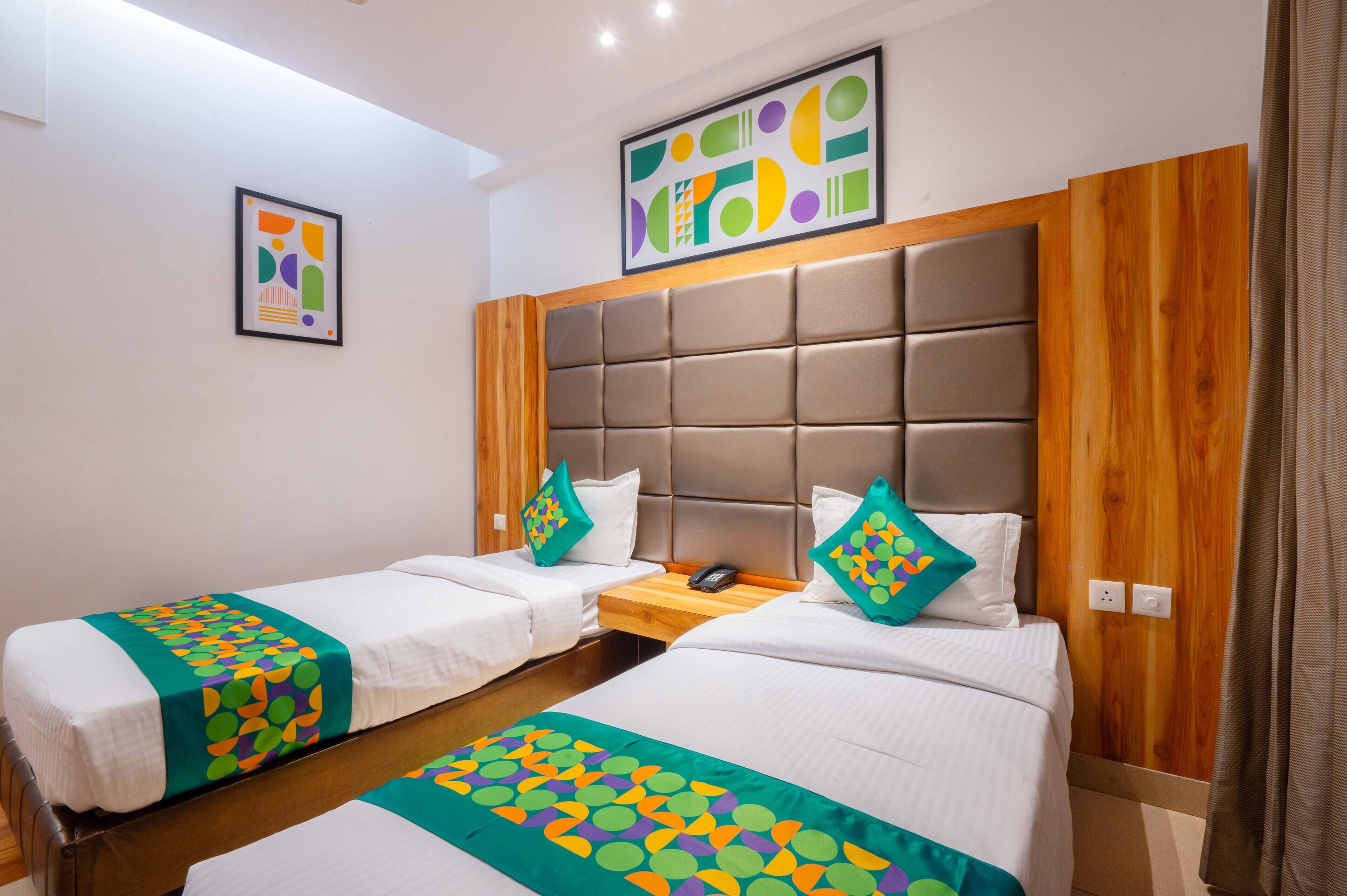 Une chambre d’hôtel avec deux lits, une tête de lit en bois, une petite table en bois et une œuvre d’art accrochée au mur.