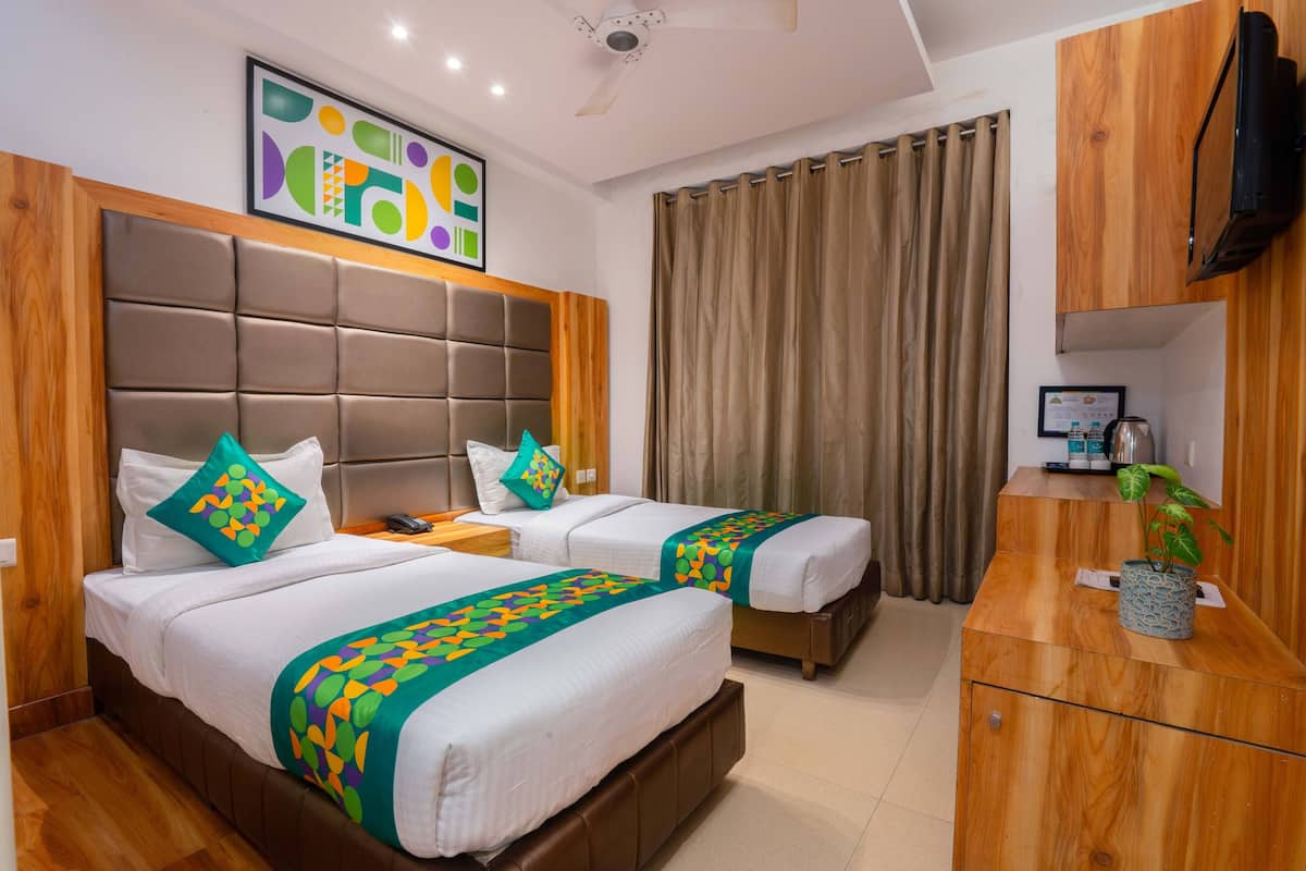 Habitación de hotel con dos camas, cabecero de madera, televisor, escritorio y una planta.