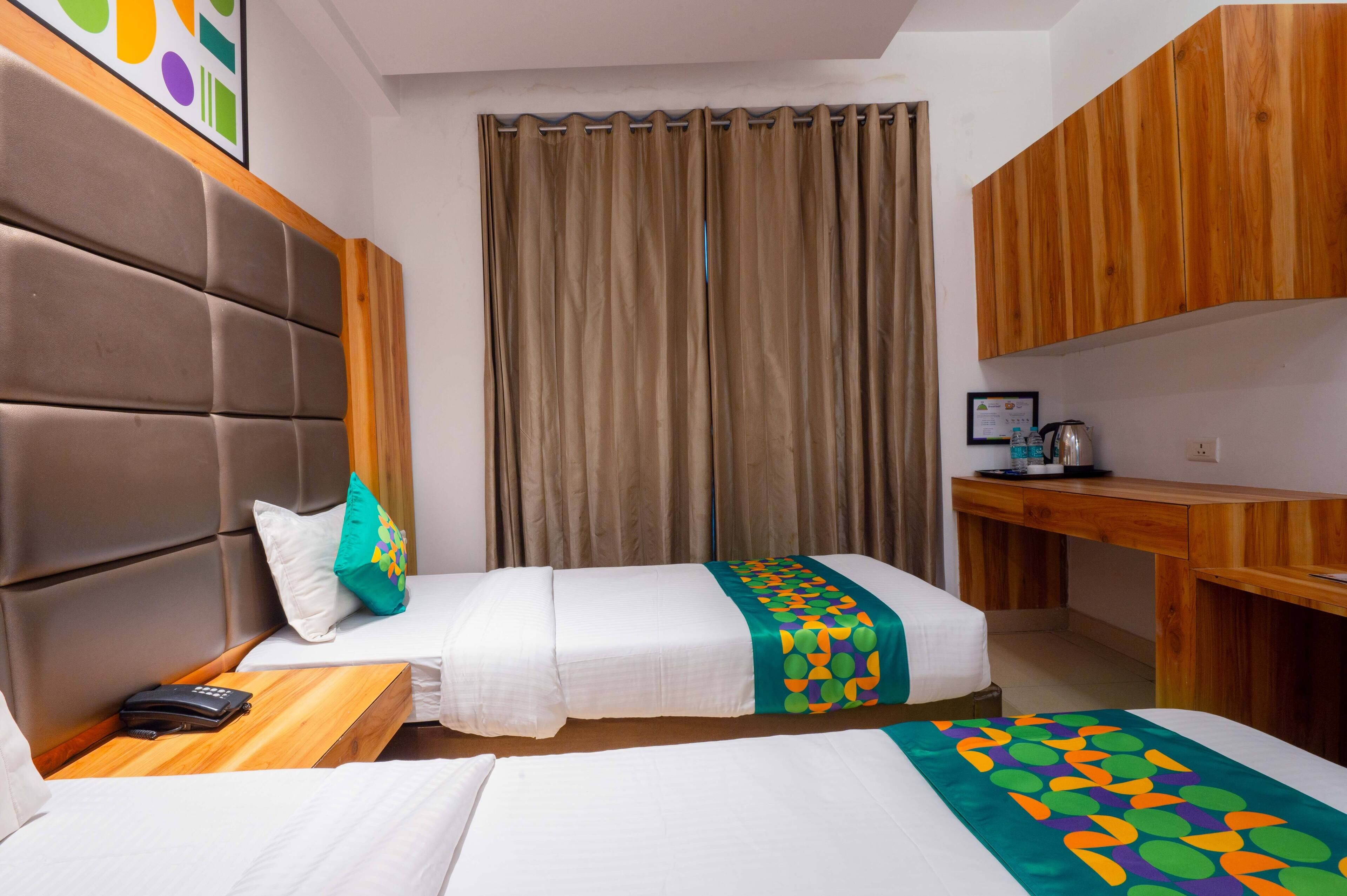 A hotel room with two beds, a wooden desk, a telephone, and a curtain.