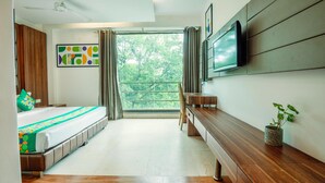 Quarto moderno com cama, televisão, um banco de madeira e janela com vista para árvores.
