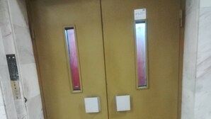 Een gesloten liftdeur met een bedieningspaneel aan de linkerkant en een bord erboven.