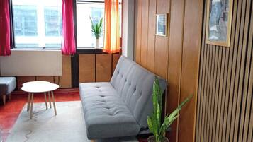 En moderne stue med en grå sofa, et lille rundt bord og en potteplante.