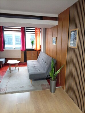 A modern living room with a grey sofa, a small round table, and a potted plant. - Cozy 1-bedroom apartment with WiFi, AC in beautiful Nis (Ниш)