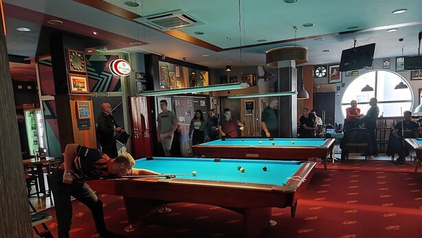 Een poolzaal met meerdere pooltafels, een klok en een bar.
