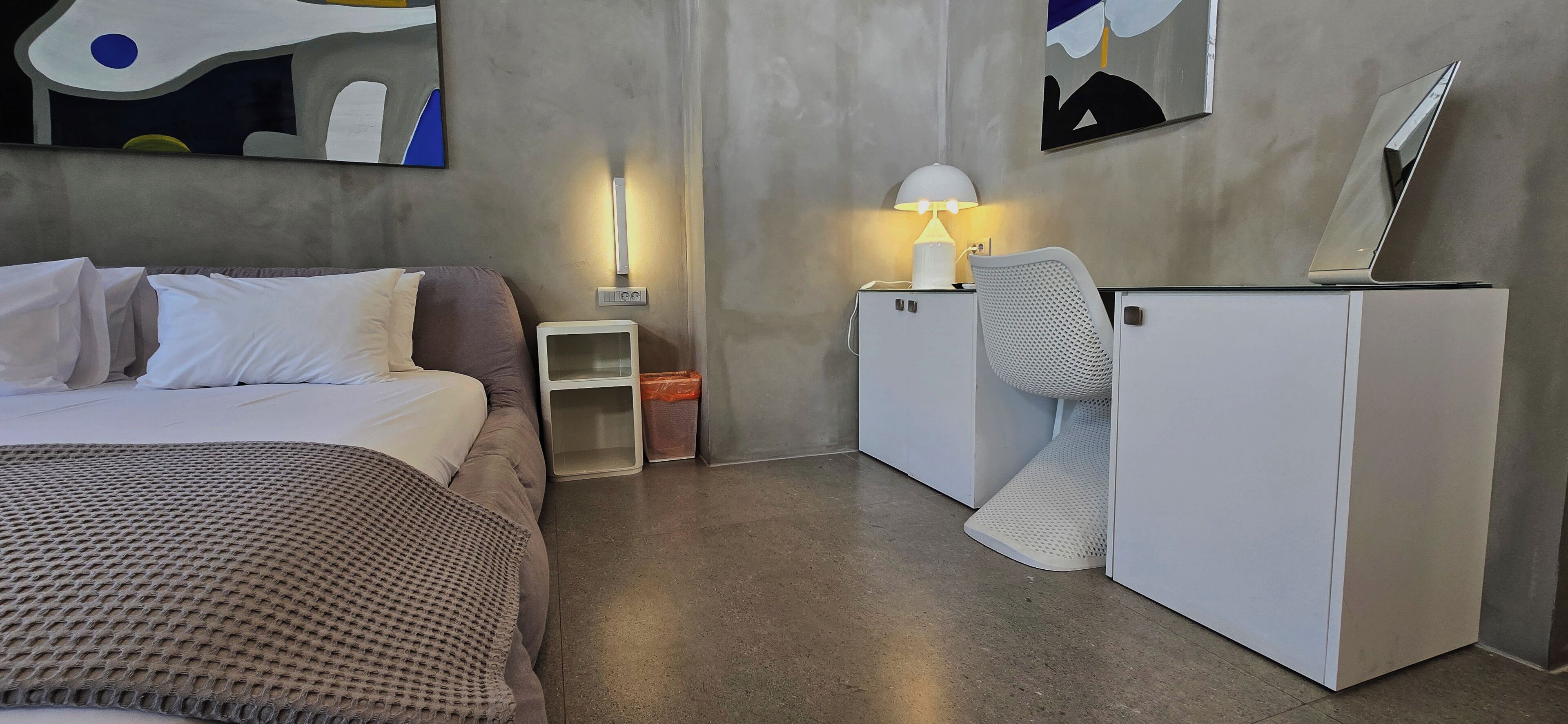 Une chambre d’hôtel moderne équipée d’un lit, d ’un bureau avec une lampe, d’un petit réfrigérateur et d’un téléviseur posé sur un meuble.